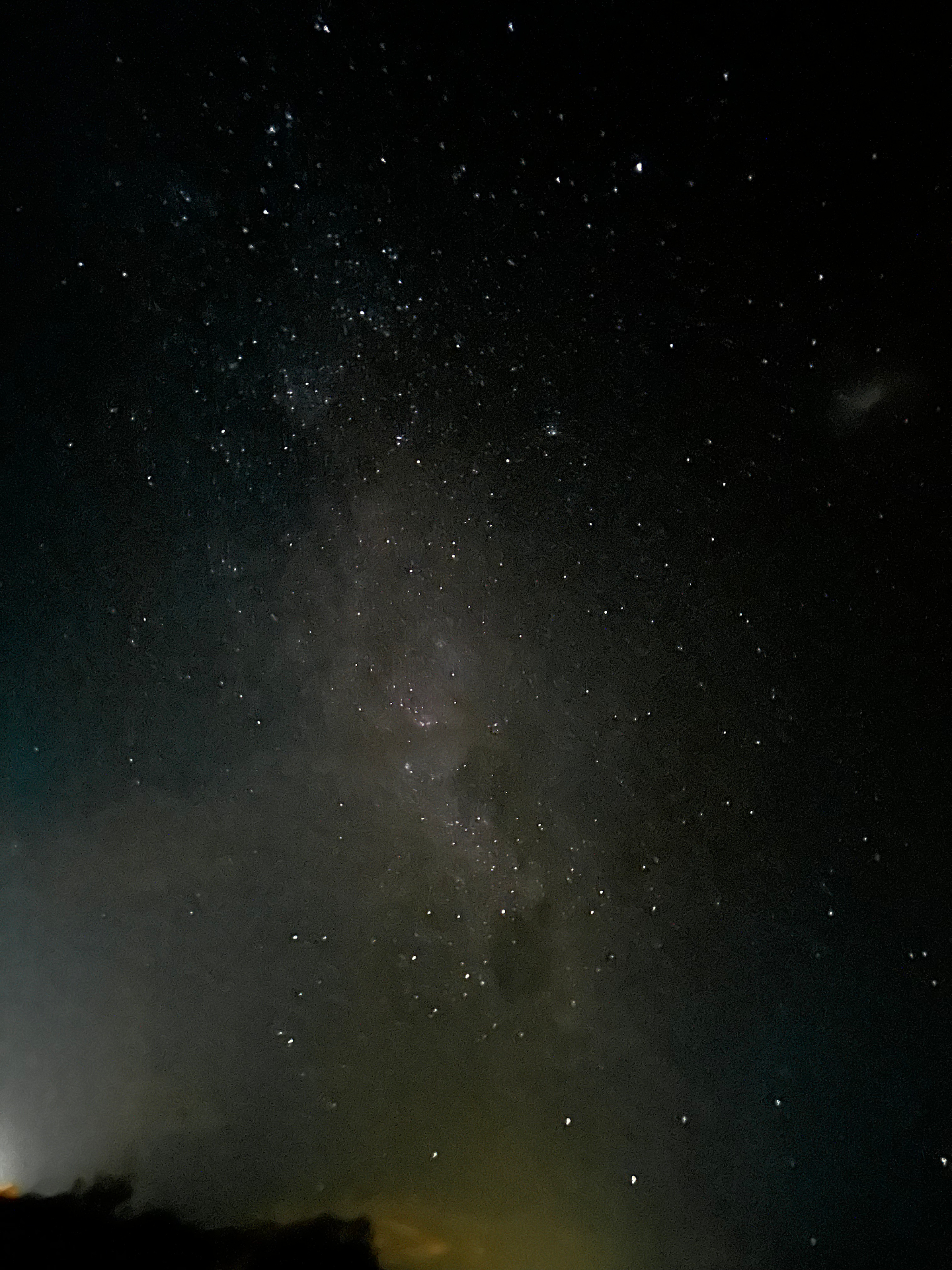 A misted Milky Way, faint pink-grey through low cloud, a single tree silhouetted at the bottom edge.